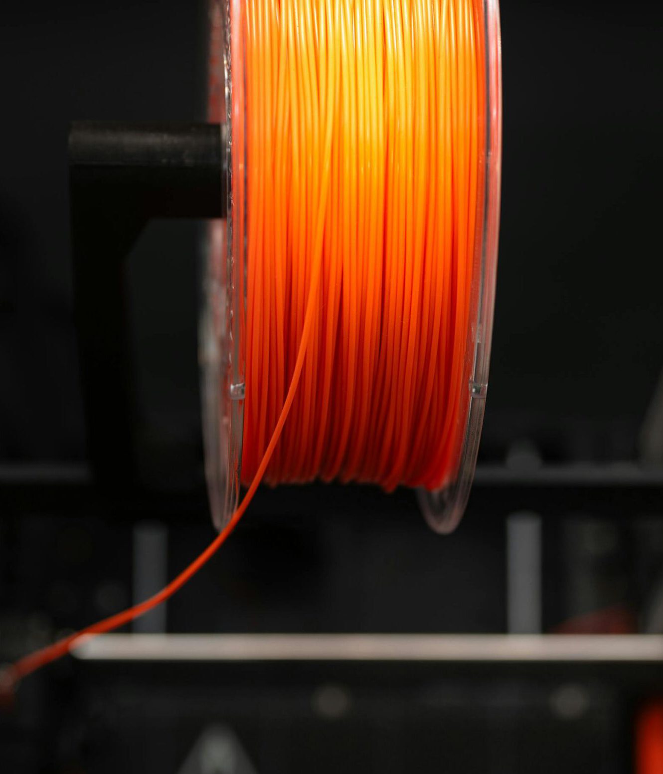 Close-up of an orange 3D printer filament spool in a workshop setting, highlighting innovation and design.